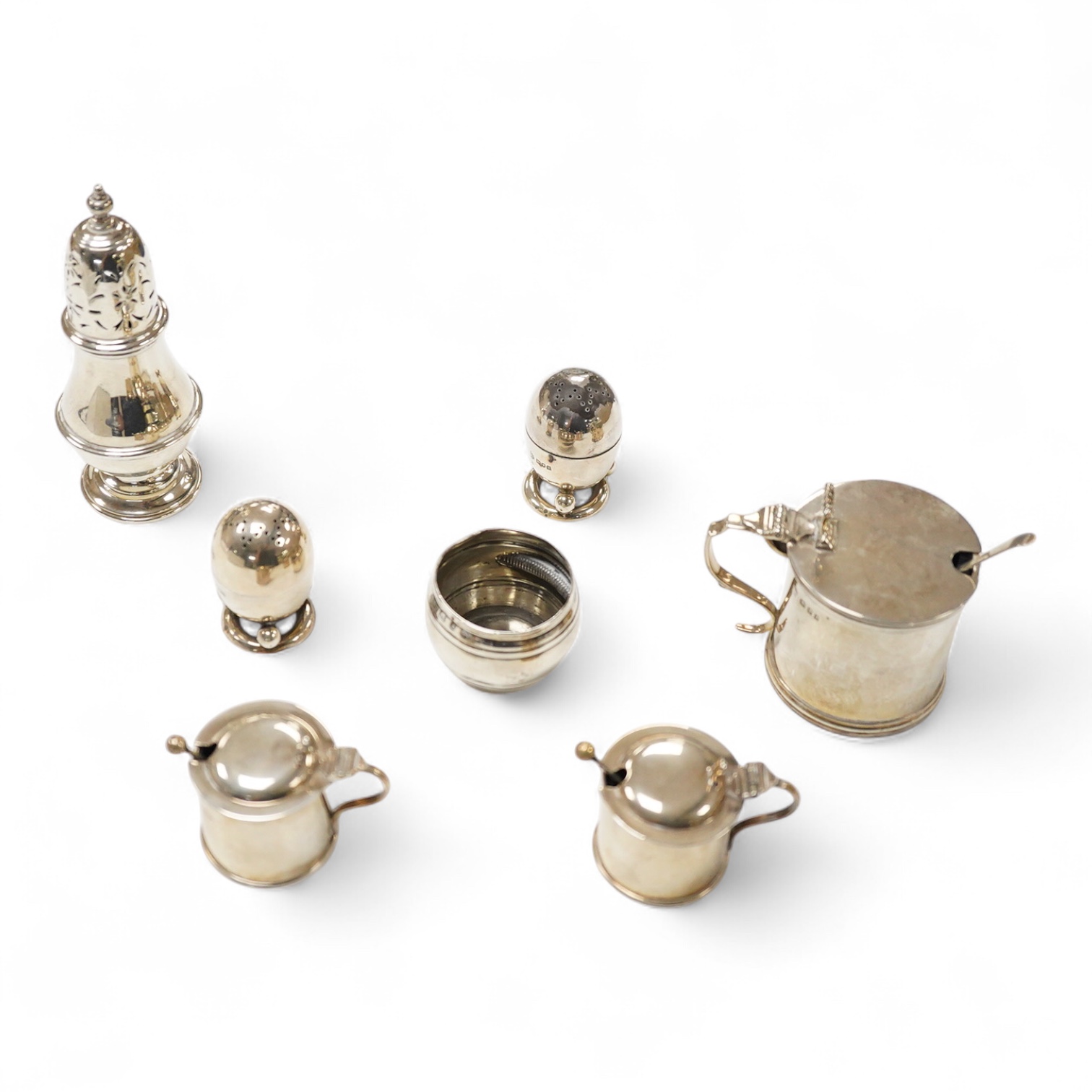 A George V silver mustard pot, London, 1931, with blue glass liner and associated silver shovel, together with a George V silver pepperette, a pair of small silver mustard pots and spoons, a pair of small silver pepperet